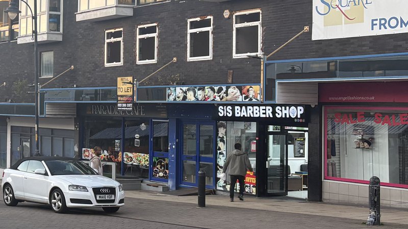 Sis Barber Shop in Old Square Shopping Centre, Walsall — black shopfront with white lettering, blue Paradise Café to the left, Angel Fashions to the right